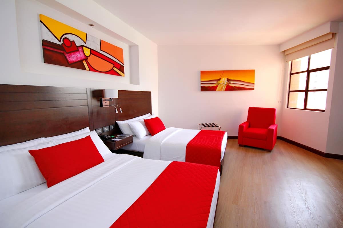 Una habitación de hotel con dos camas, una silla roja, obras de arte en las paredes y un ventanal.