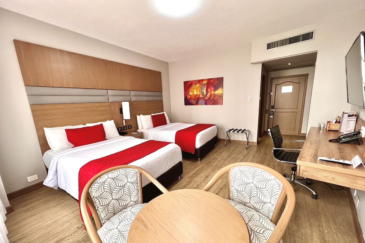 Una habitación de hotel con dos camas, un escritorio, una silla y un cuadro en la pared.