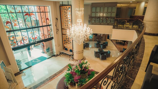 En hotellobby med en prangende lysekrone, siddeområde og en dekorativ plante i midten.