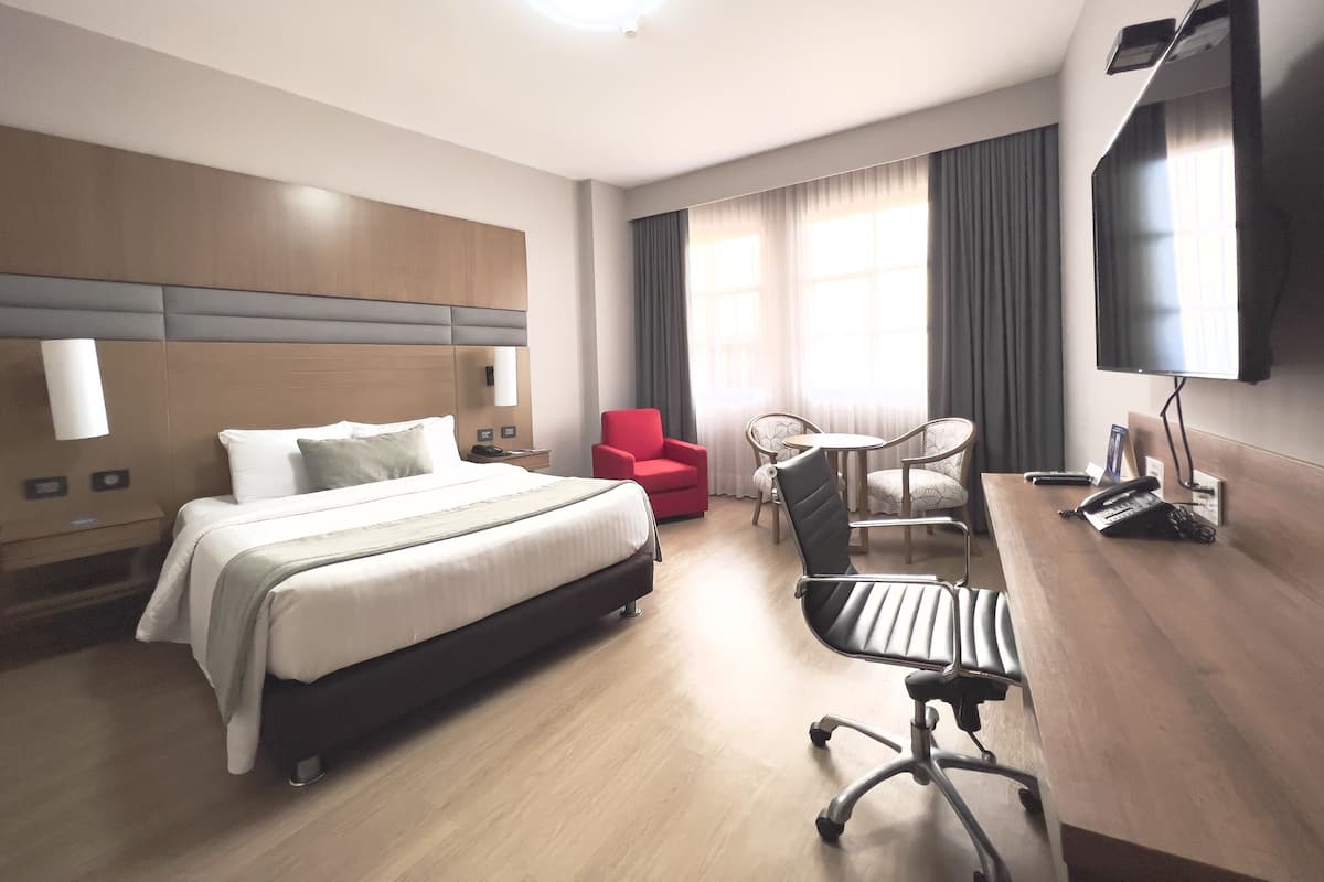 Habitación de hotel con cama, escritorio con silla, televisor y ventana con cortinas.