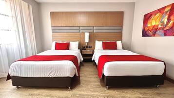 Habitació d'hotel amb dos llits, un panell de capçalera de fusta, un quadre a la paret i una finestra amb cortines.