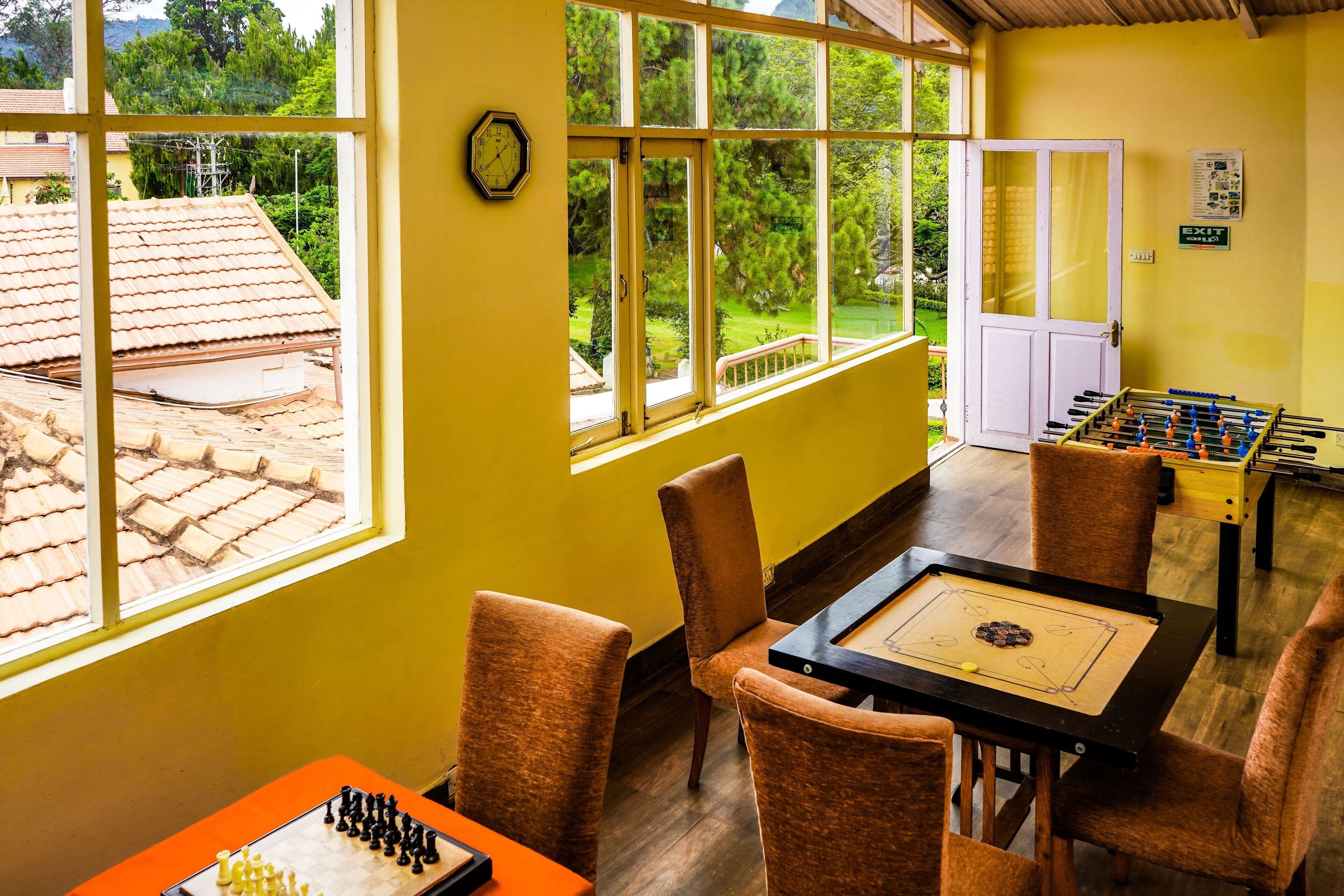 A room with a foosball table, a chessboard, and a window with a view of a house and trees.