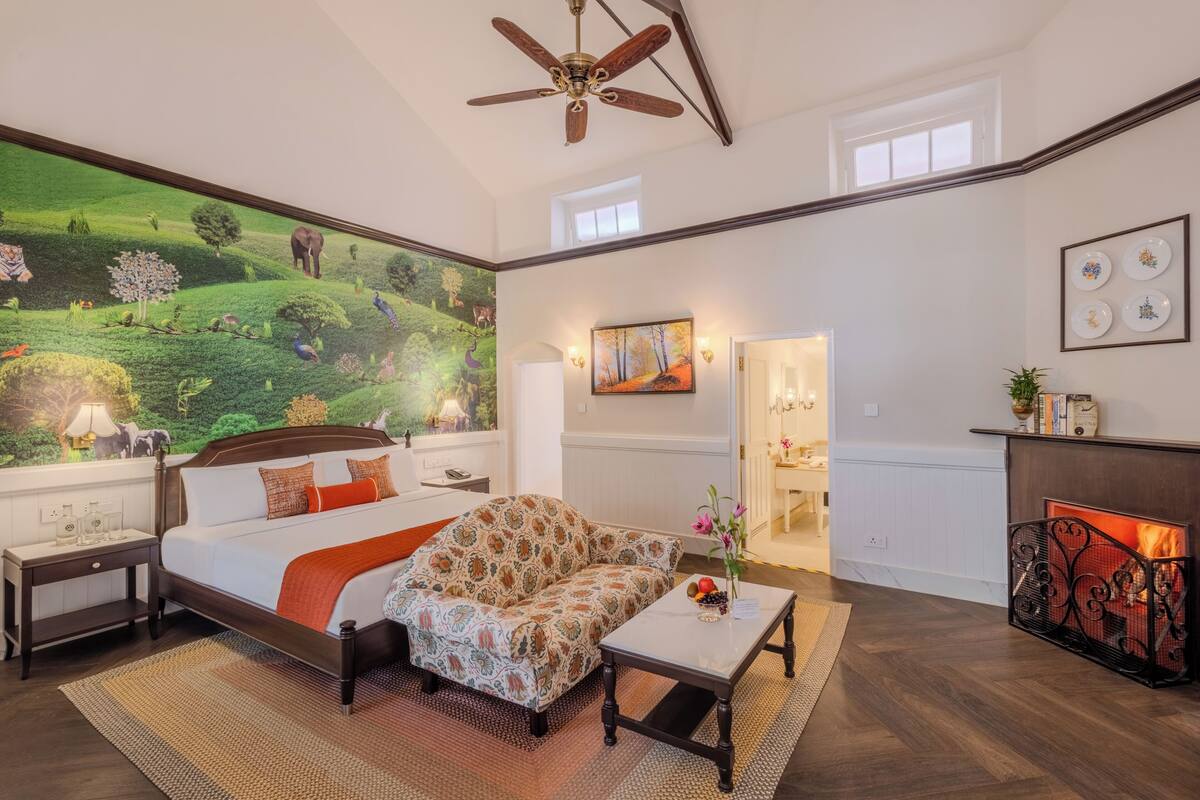 A bedroom with a large mural, a bed, a sofa, a fireplace, and a ceiling fan.