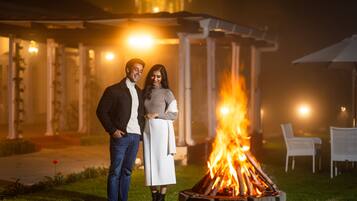 A couple standing by a fire pit in an outdoor setting with a gazebo and chairs in the background.
