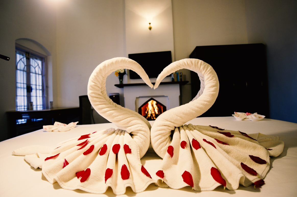Una cama con toallas dispuestas en forma de cisnes, una chimenea y una ventana con vistas al exterior.