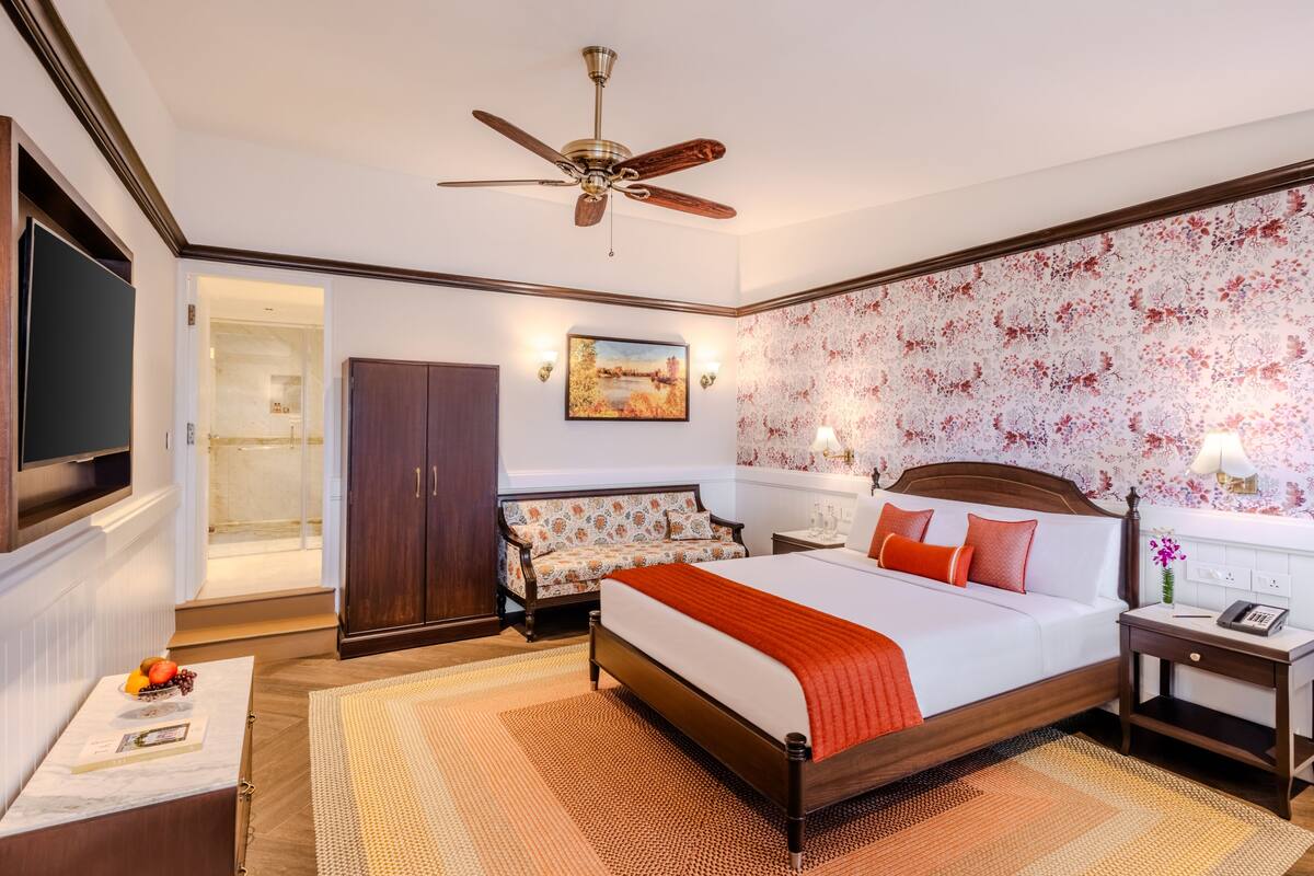 A hotel room with a bed, a desk, a wardrobe, a TV, and a ceiling fan.