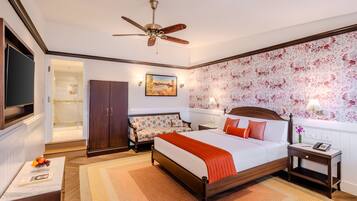 A hotel room with a bed, a desk, a wardrobe, a TV, and a ceiling fan.
