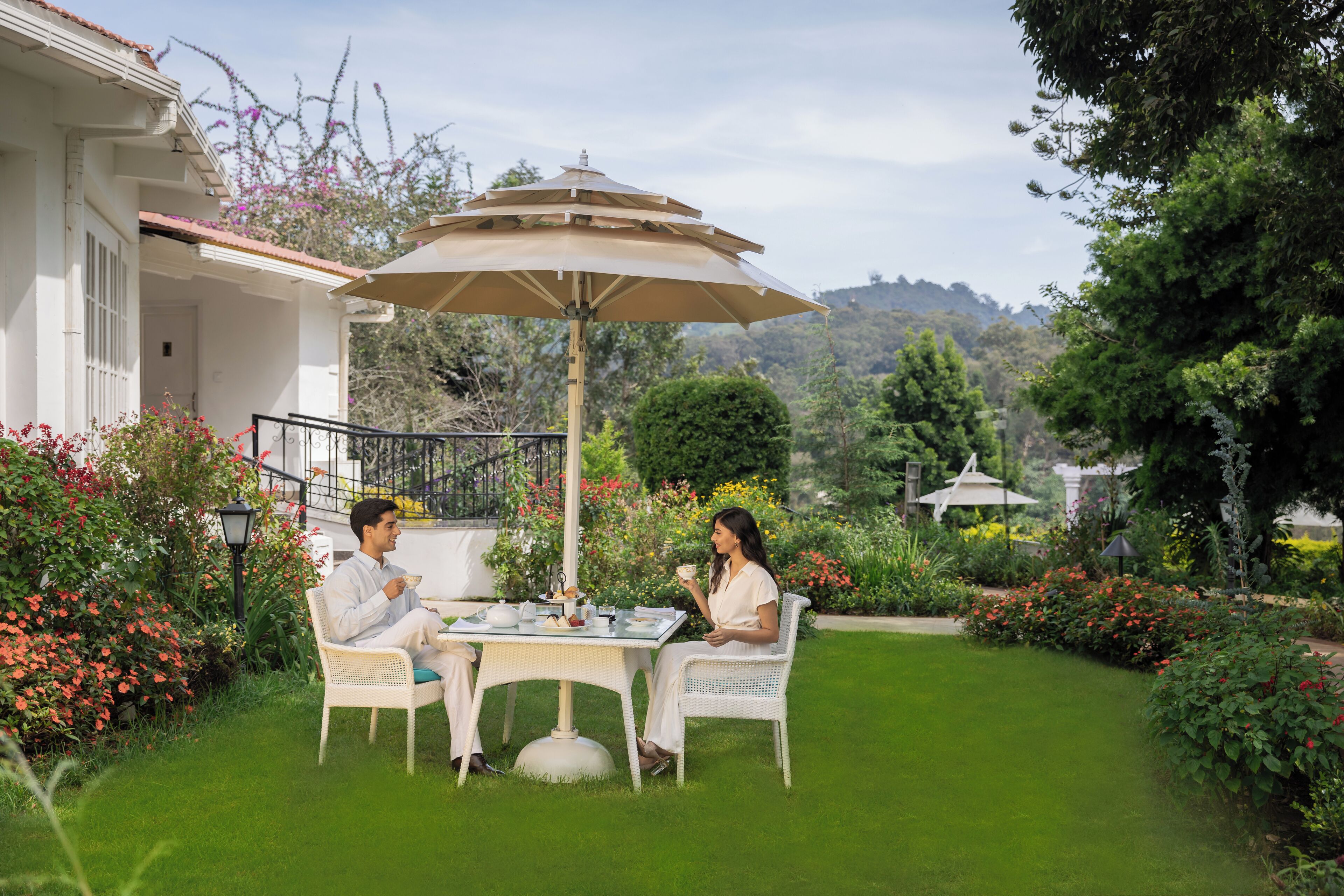 A patio with a table and chairs, surrounded by lush greenery and flowers.