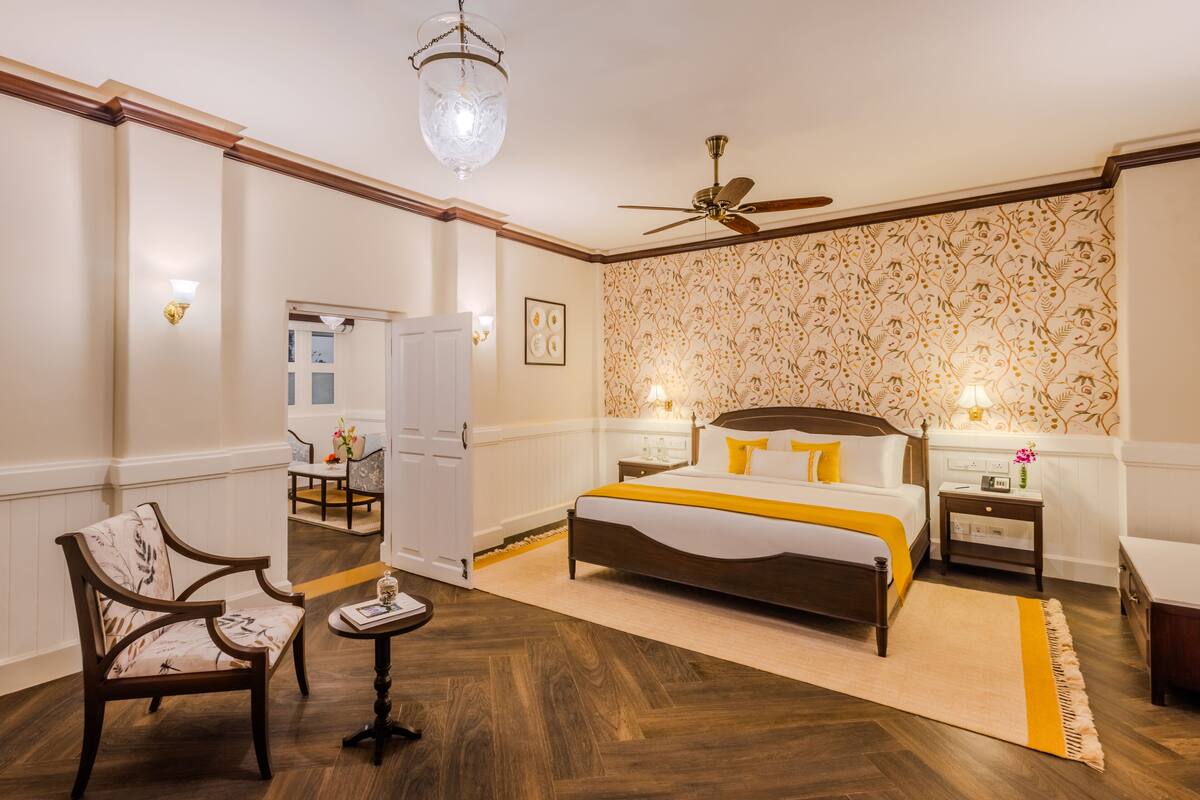 A hotel room with a large bed, two bedside tables, a chair, a desk, a ceiling fan, and a chandelier.