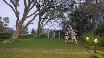 Relax in a serene garden setting surrounded by lush trees and a tranquil lawn, featuring a central swing set.