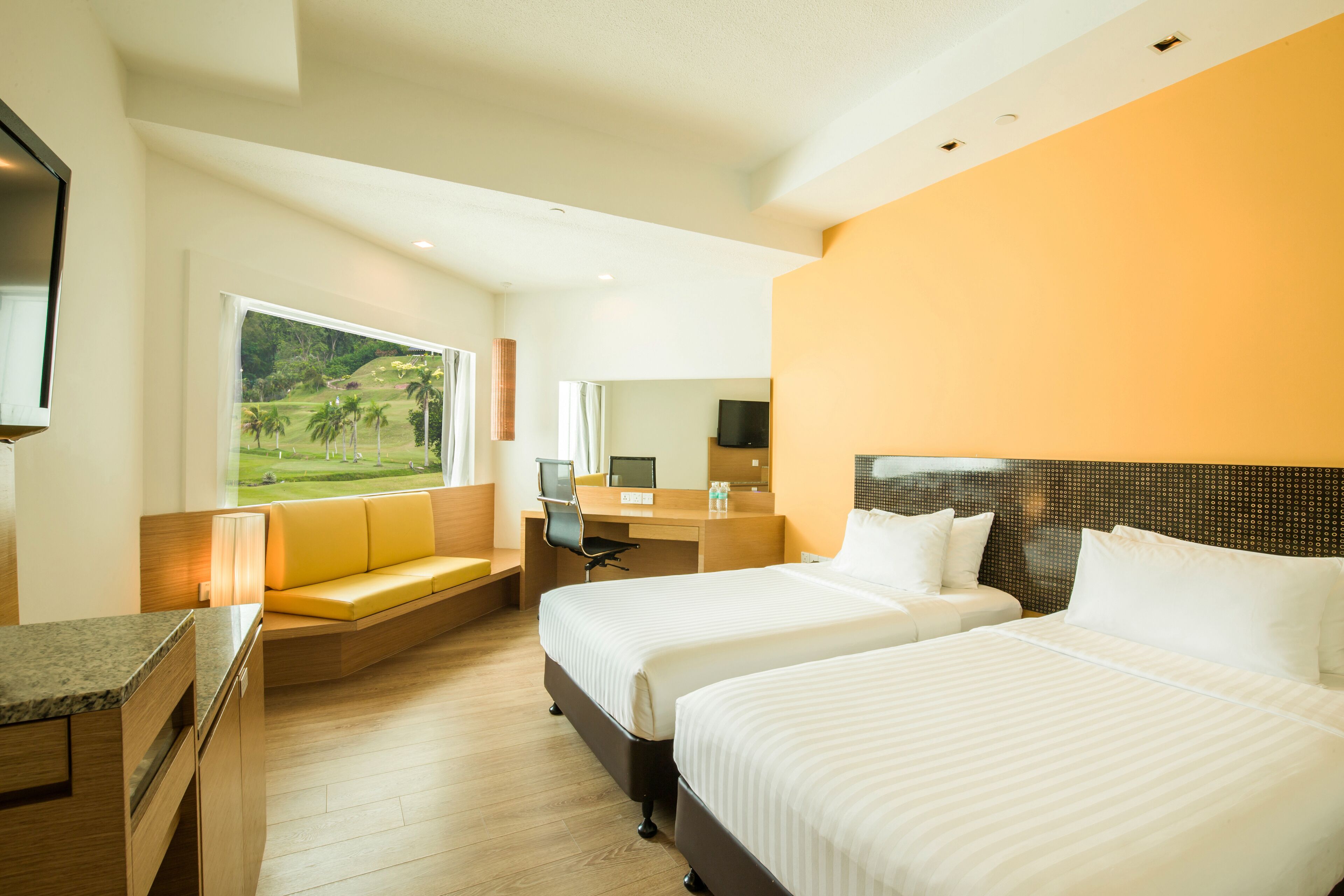 Habitación de hotel con dos camas, un escritorio, un sofá, un televisor y una ventana con vistas a zonas verdes.