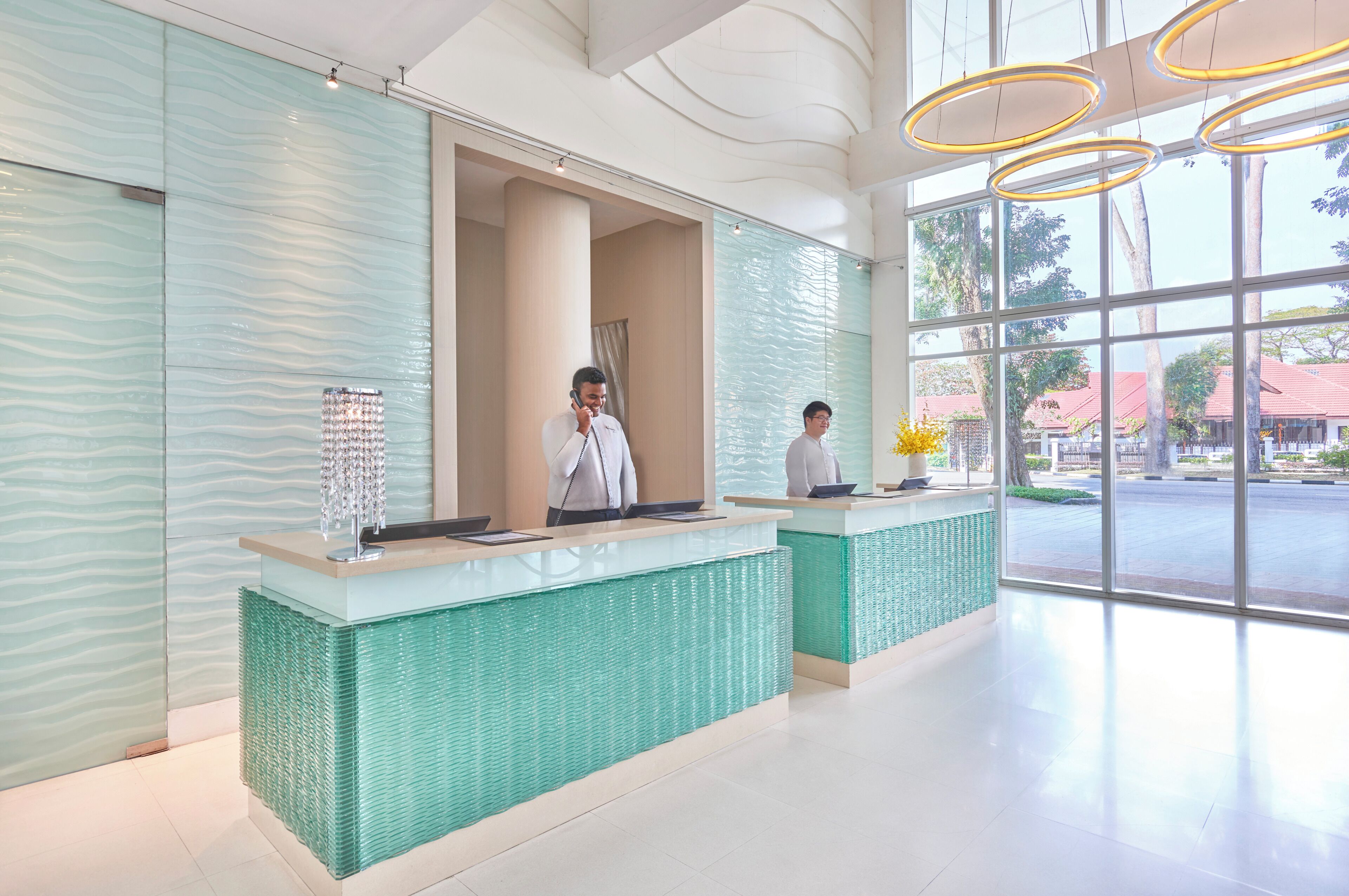A reception area with a glass wall, a reception desk, and a large window with a view of buildings and trees.