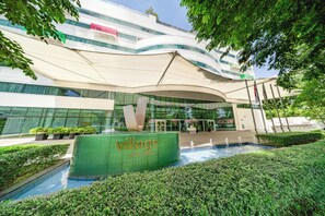 Une entrée d'hôtel moderne, avec une grande enseigne indiquant « VILLAGE HOTEL CANTAGI », un espace piscine et une végétation bien entretenue.