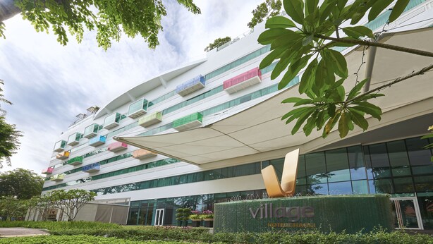 A modern hotel with a multi-story structure, balconies with colorful railings, and a prominent entrance with a green hedge.