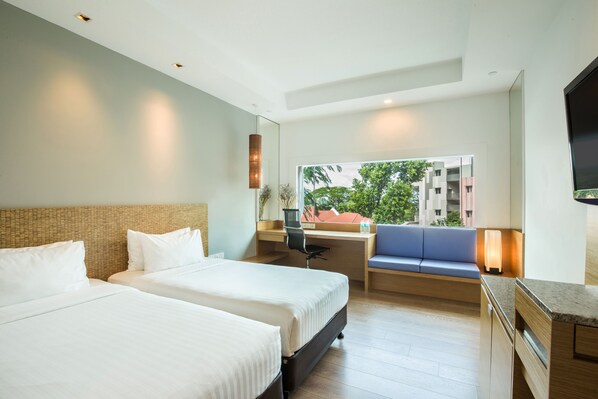 A hotel room with two beds, a desk, a chair, a sofa, and a TV.