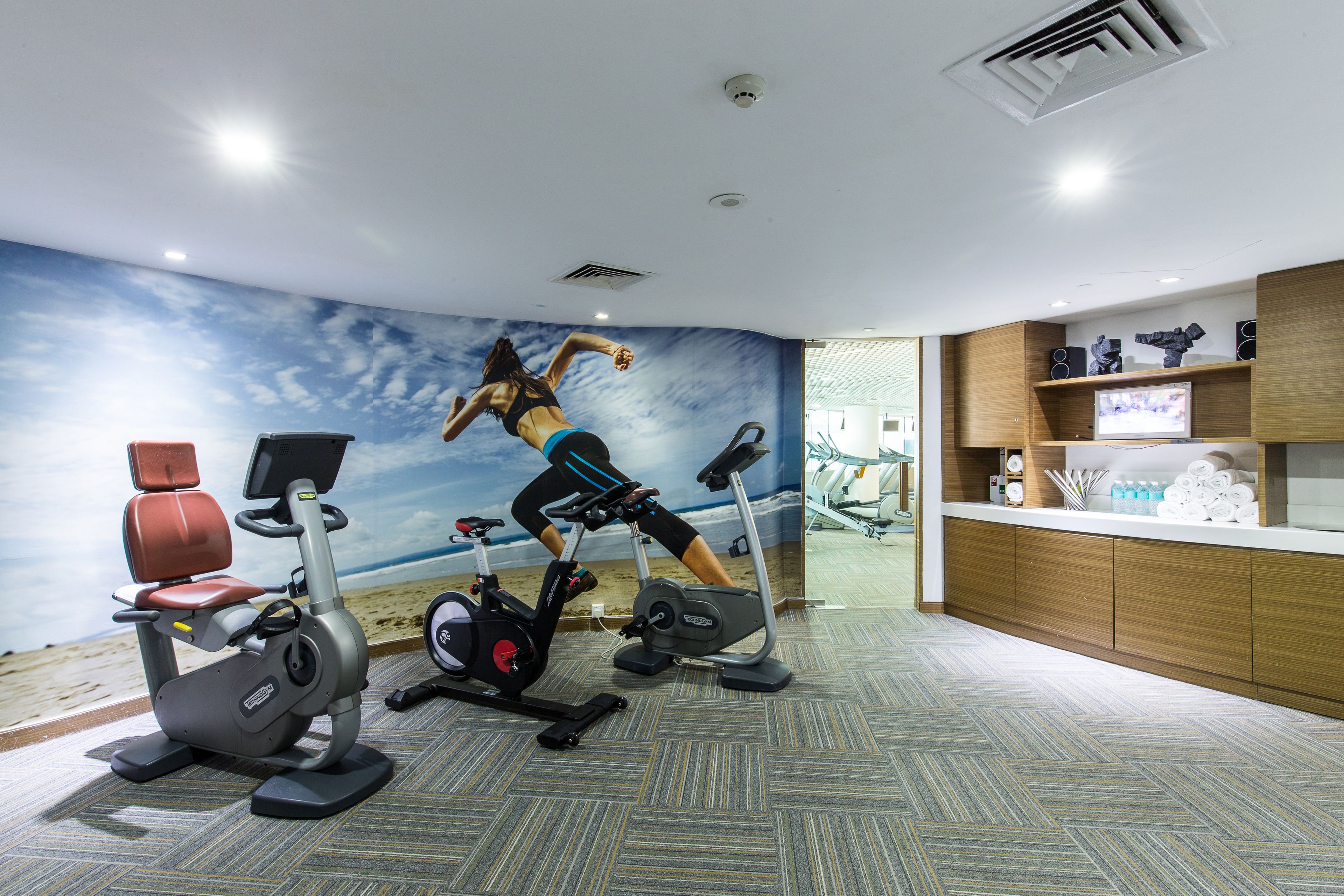 A gym with stationary bikes, a rowing machine, and a wall mural of a runner.