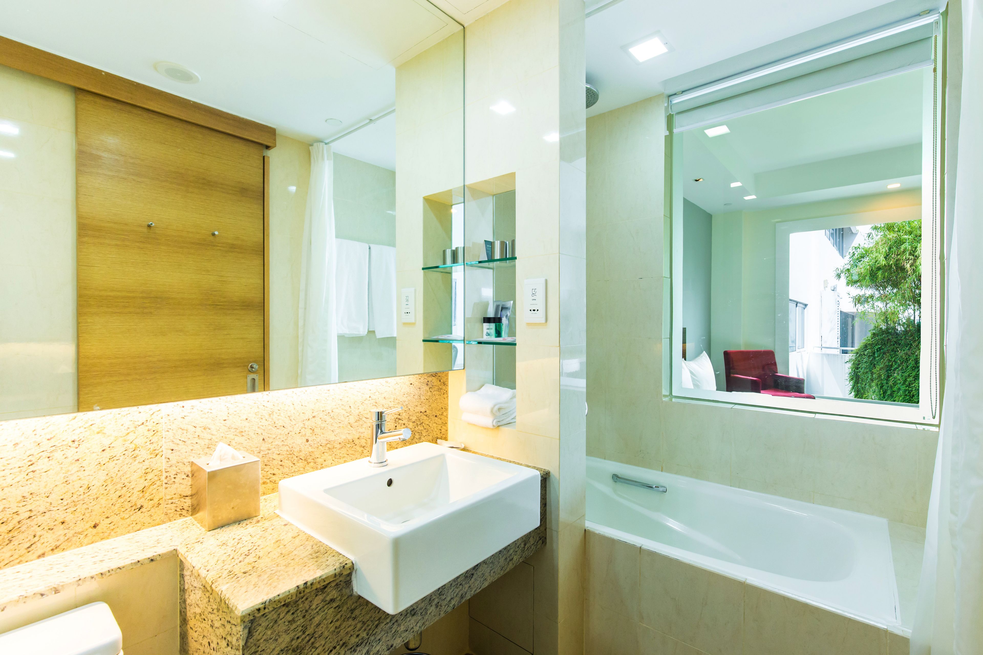 A modern bathroom with a granite countertop, a white sink, a glass shower enclosure, and a large mirror.