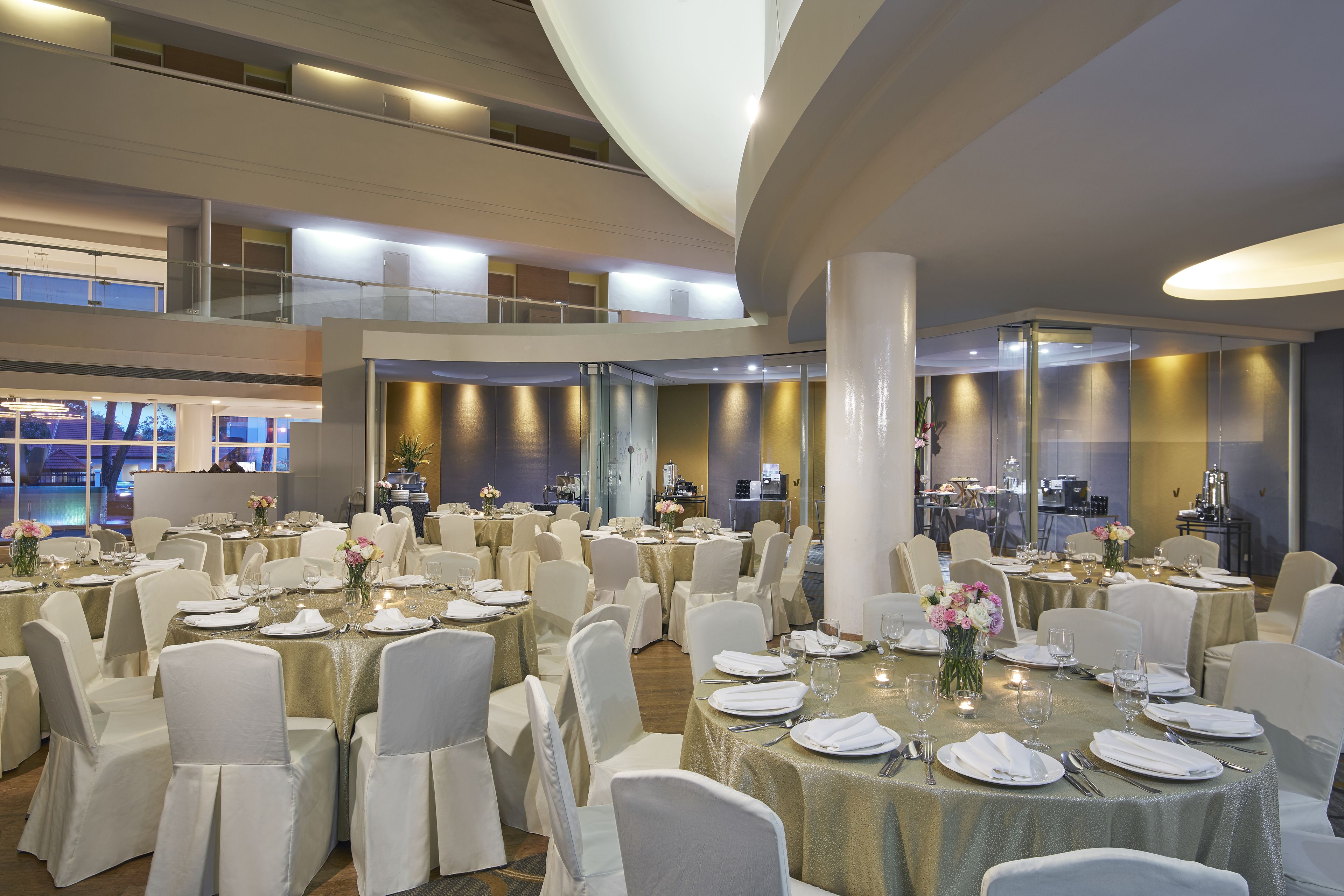 Un amplio salón de banquetes con varias mesas redondas dispuestas para comer, rodeado de sillas blancas.