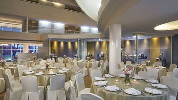 Un amplio salón de banquetes con varias mesas redondas dispuestas para comer, rodeado de sillas blancas.
