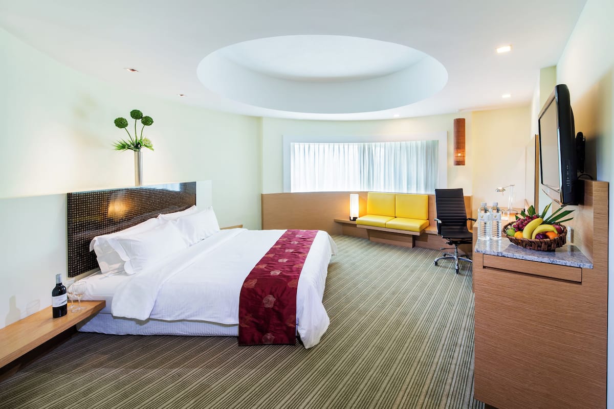 A modern hotel room with a large bed, a desk with a computer, a seating area, and a TV.