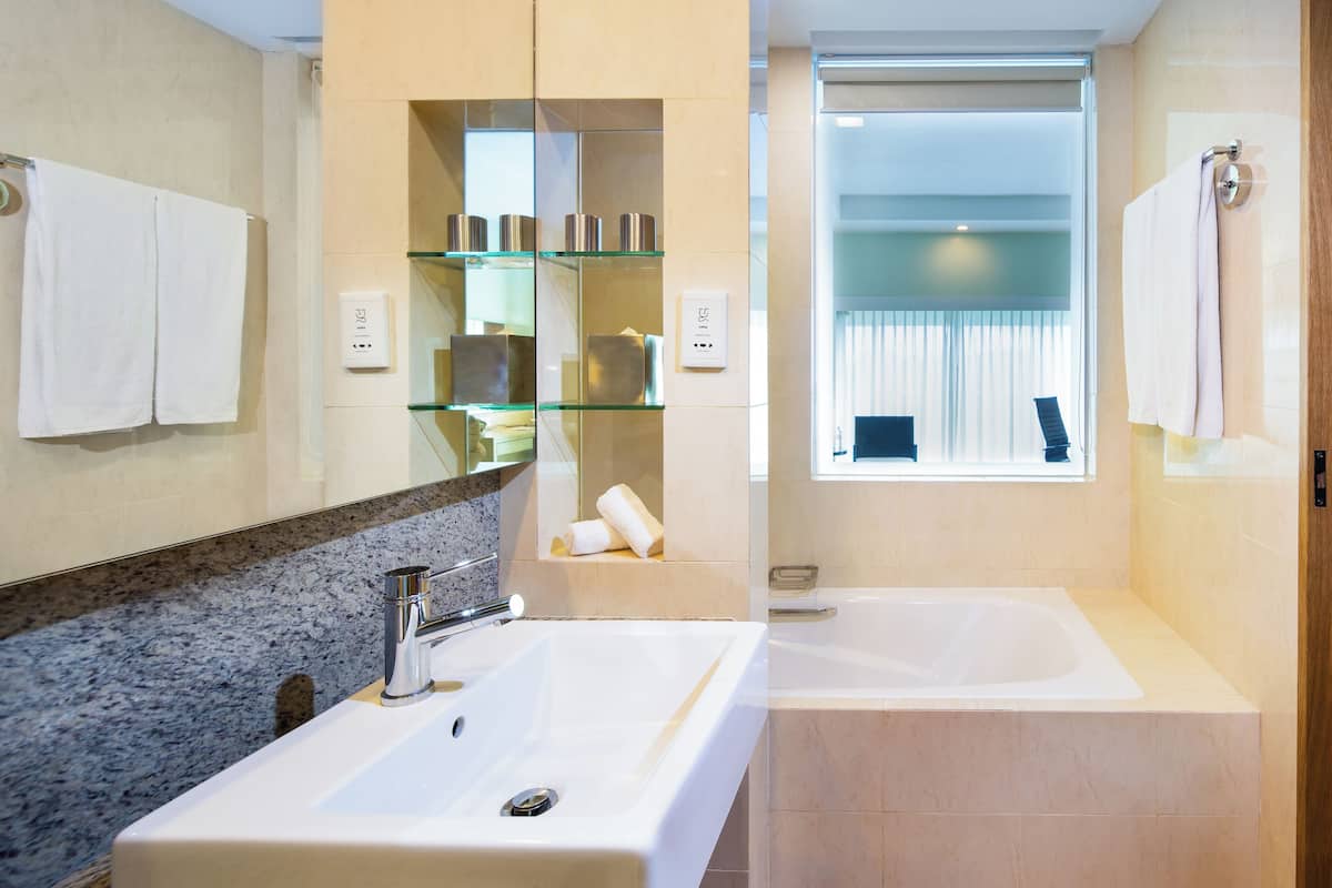 A modern bathroom with a large sink, a bathtub, and a glass shelf with toiletries.