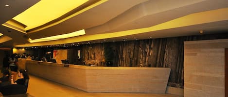 A modern reception area with a curved counter, a stone wall backdrop, and a wooden floor.
