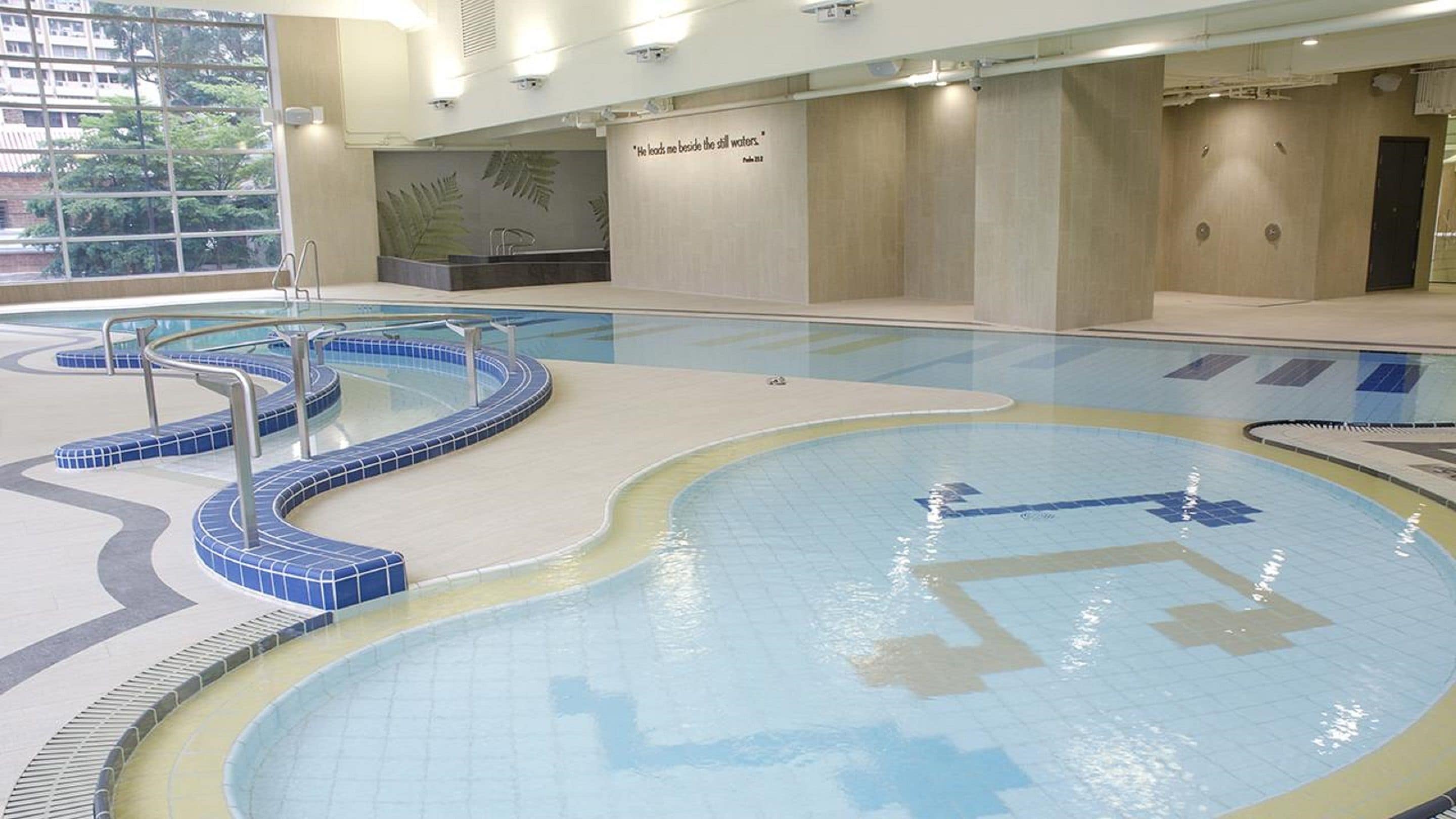 An indoor swimming pool with a blue and white tiled design, a glass barrier, and a wall with a quote.