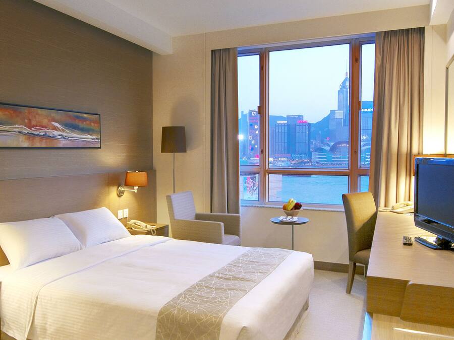 A hotel room with a large bed, a desk with a TV, a chair, a small table with fruit, and a painting on the wall.