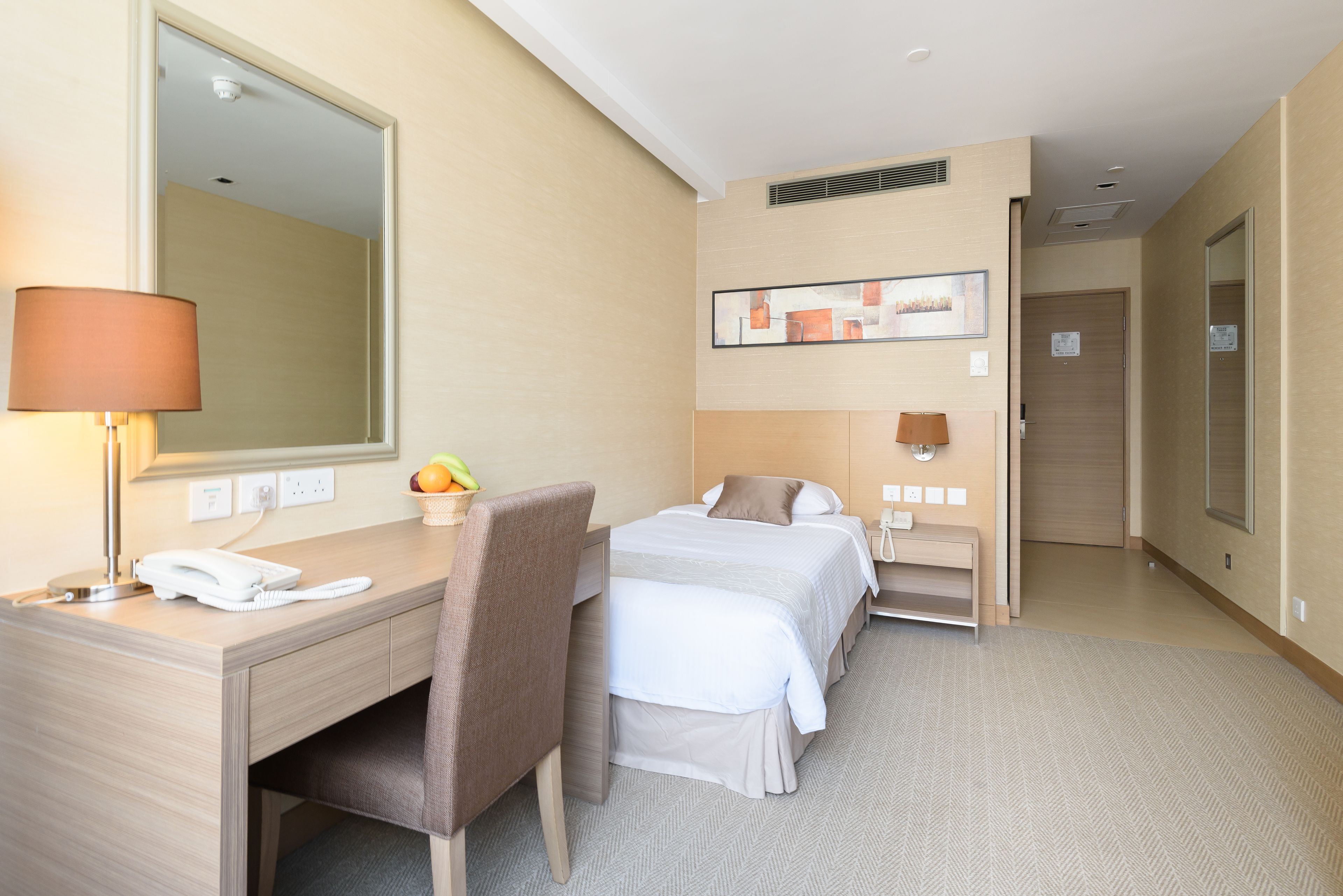 A hotel room with a desk, two beds, a mirror, a lamp, and a fruit bowl.