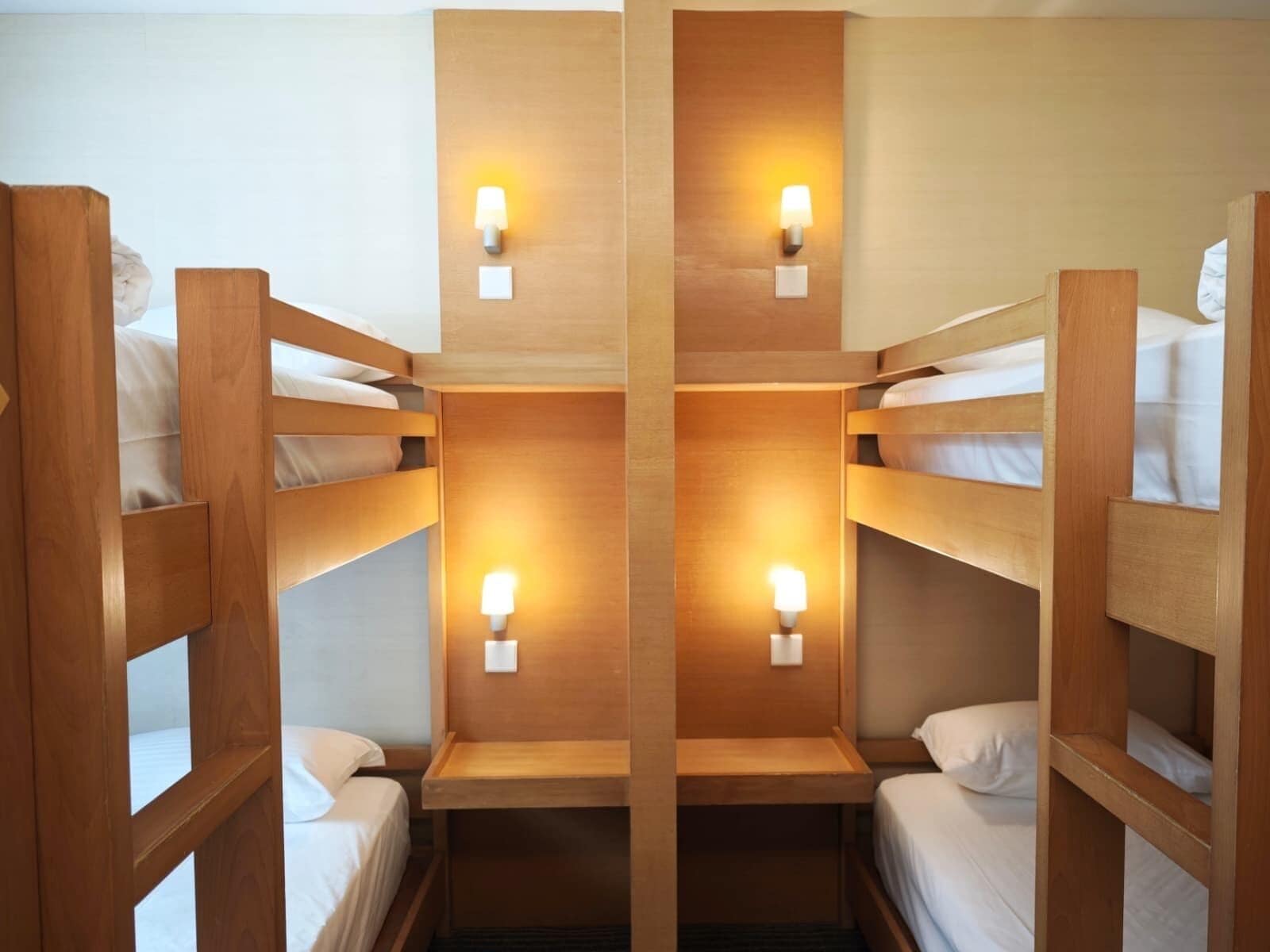 A room with four wooden bunk beds, each with a bedside table and a wall-mounted light.