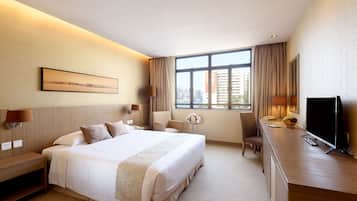 A hotel room with a large bed, a desk, a TV, and a window with a city view.