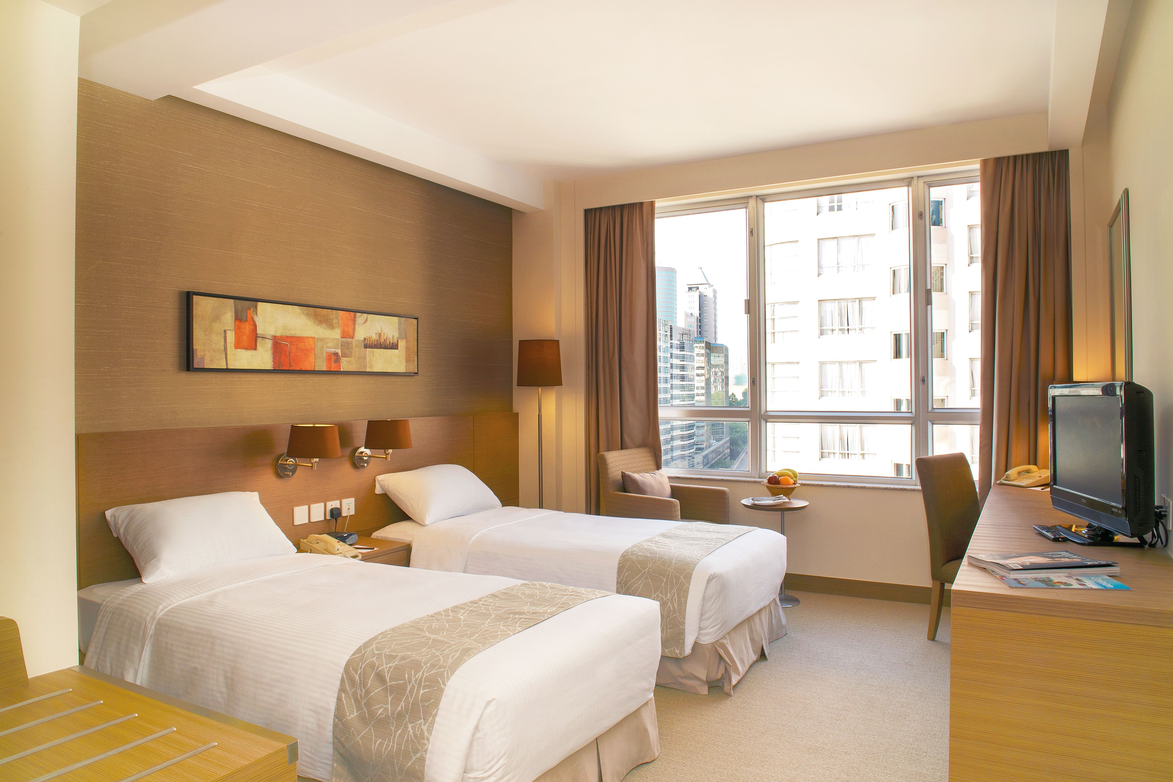 A hotel room with two beds, a desk with a computer, a chair, a small table, and a window with curtains.