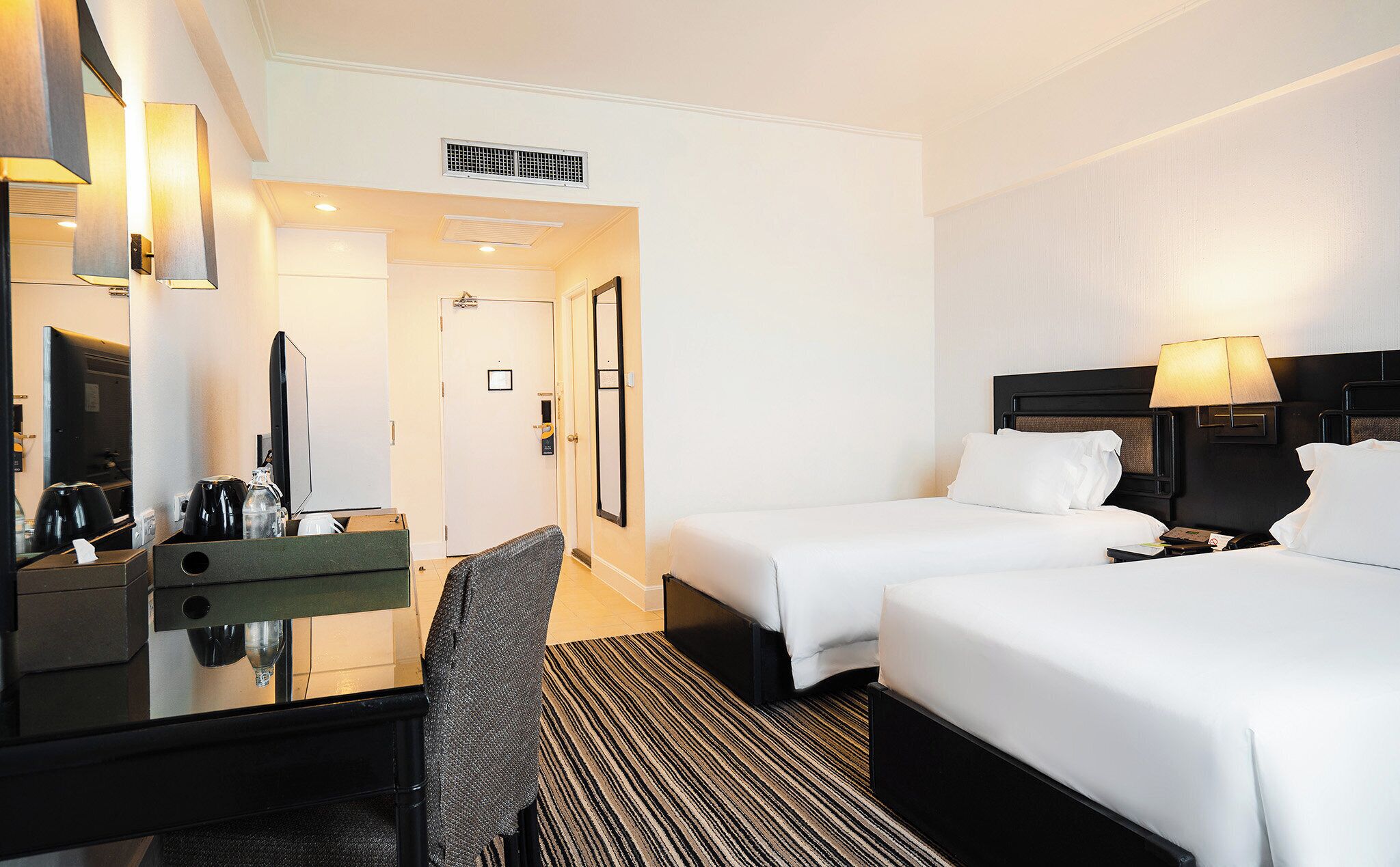 A hotel room with two beds, a desk with a mirror, a chair, and a coffee machine.