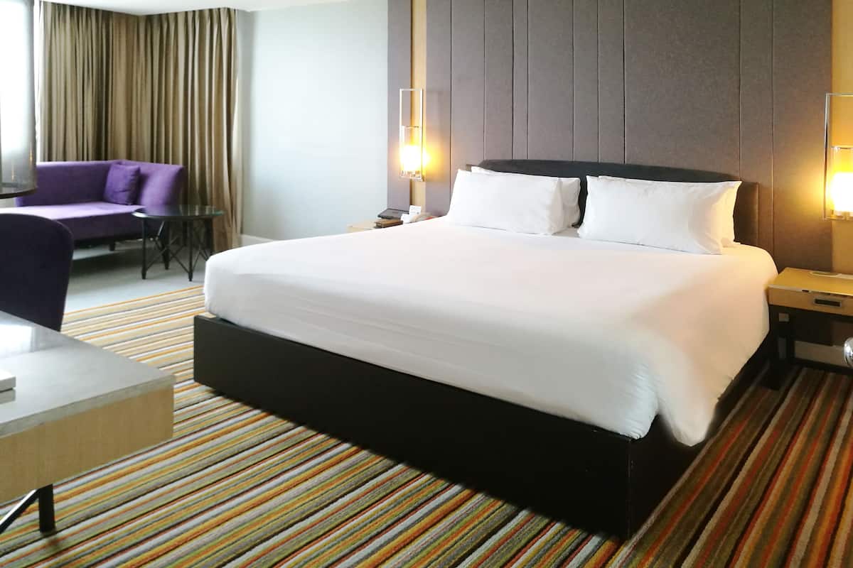A hotel room with a large bed, a small table, a chair, and a sofa.