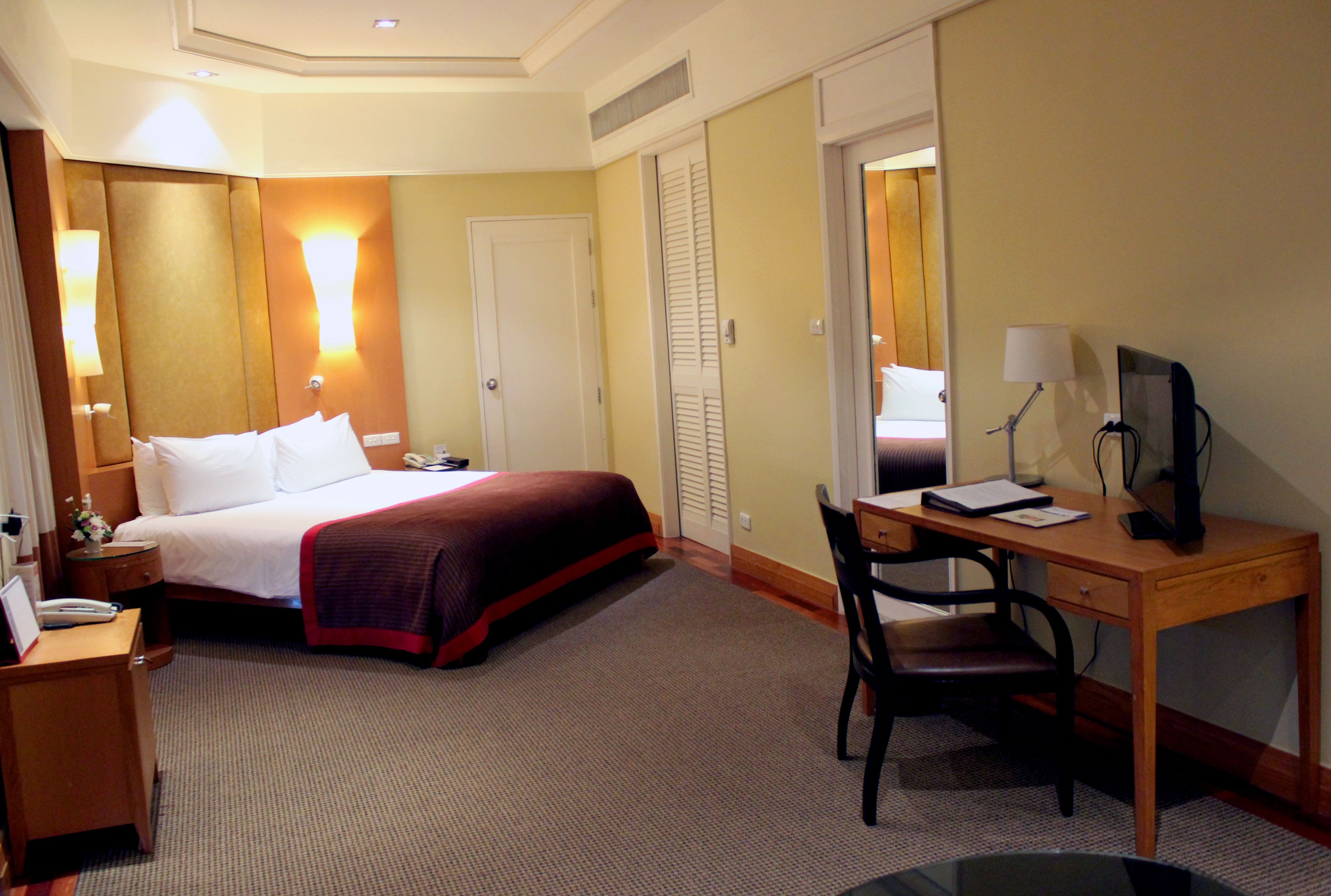 A hotel room with a bed, desk, chair, lamp, and a mirror.