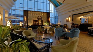 Eine geräumige Lobby mit hoher, gewölbter Decke, großen Fenstern und verschiedenen Sitzgelegenheiten, darunter Sofas und Sessel.