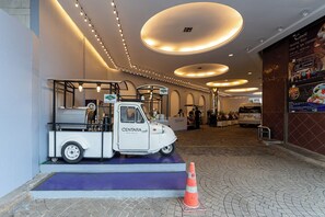 L’entrée d’un hôtel, avec un camion blanc arborant le logo de la chaîne Centara, un espace recouvert d’un tapis violet et un sol carrelé.