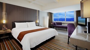 Ein Hotelzimmer mit einem großen Bett, einem Schreibtisch, einem Sessel und Blick auf die Berge.