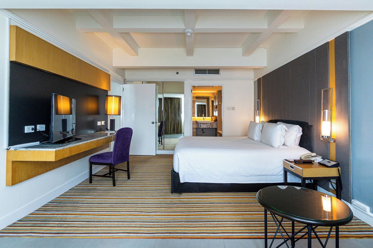 Een hotelkamer met een bed, een bureau met stoel, een televisie en een badkamer door een open deur.