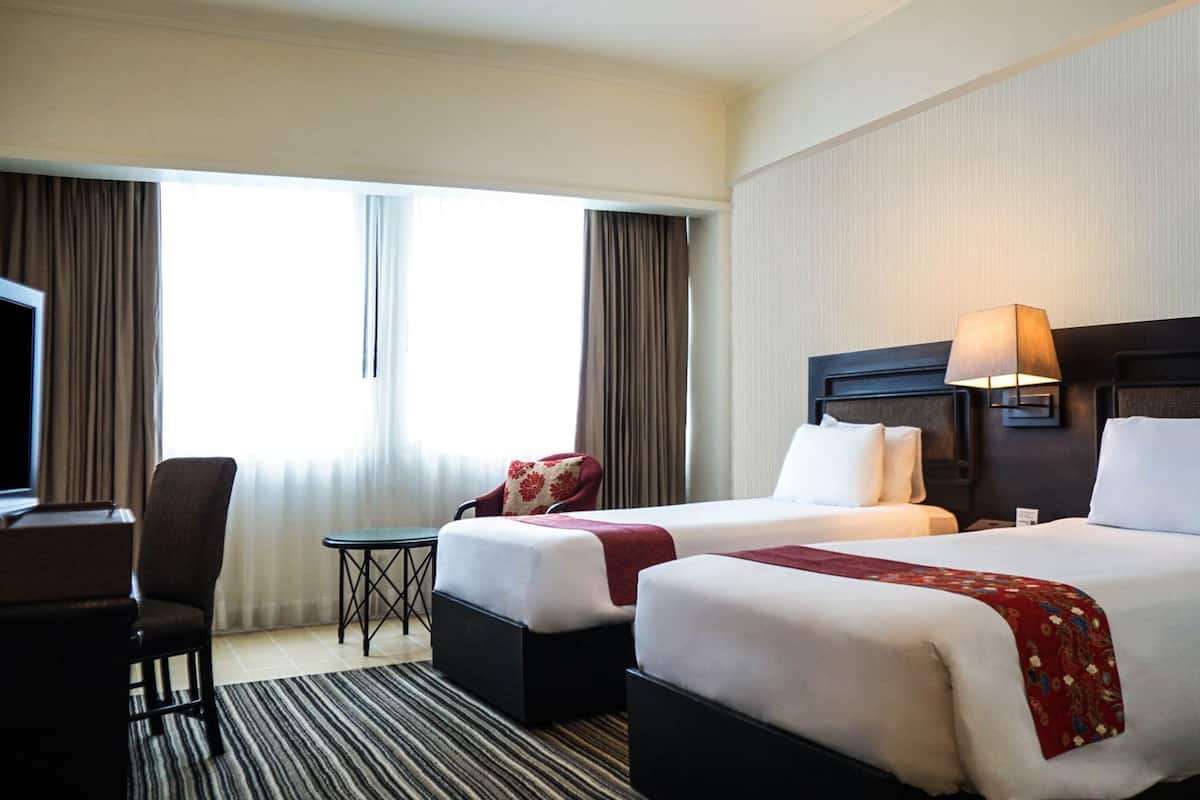 A hotel room with two beds, a TV, a desk, and a small table.
