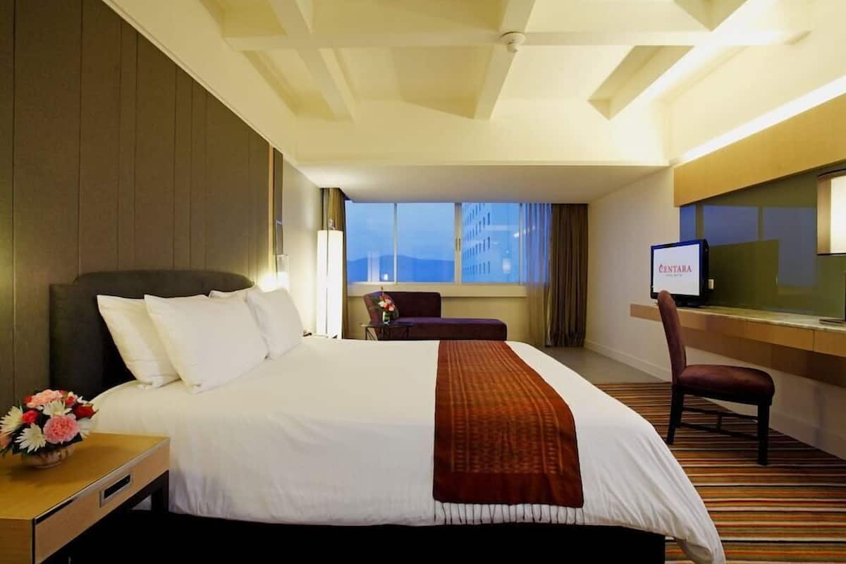 A hotel room with a large bed, a desk with a computer, a chair, and a window with a view.