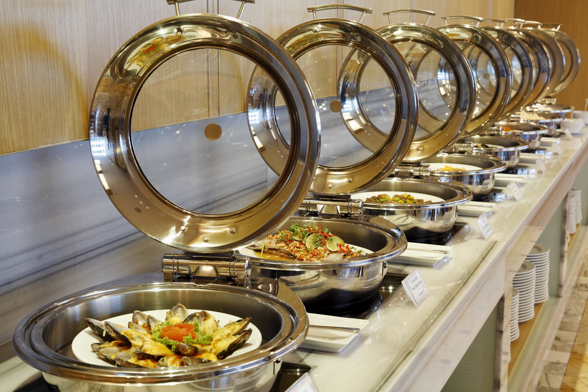 A buffet line with various dishes, including seafood and salads, in stainless steel serving dishes.