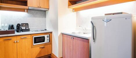 A compact kitchen with wooden cabinets, a built-in microwave, a refrigerator, and a coffee maker.