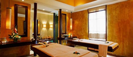 A spa room with two massage tables, a large mirror, and a window providing natural light.