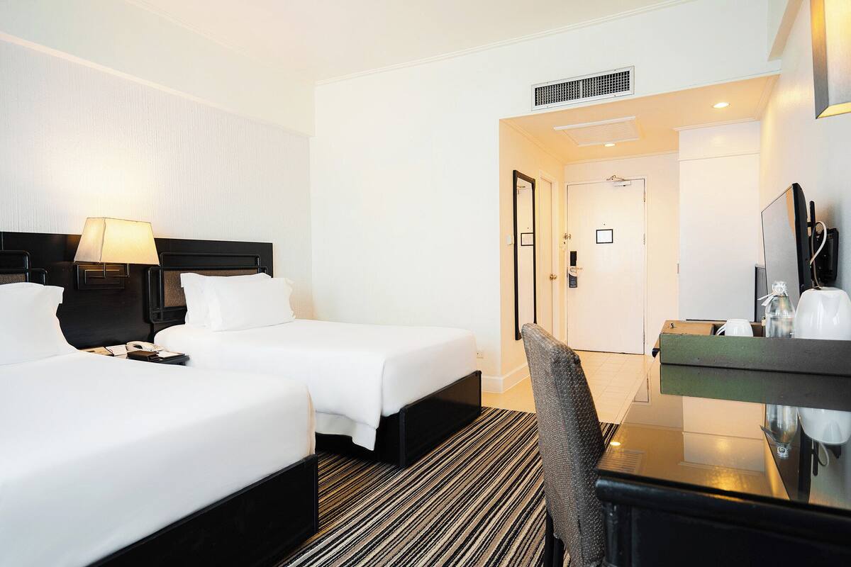 A hotel room with two beds, a desk with a mirror, a lamp, and a coffee machine.
