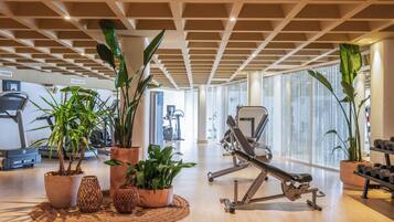 Un gimnasio con equipo de ejercicio, plantas en macetas y ventanas amplias.