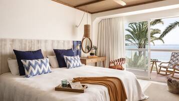 A bedroom with a large bed, a bedside table, a chair, and a view of the ocean.