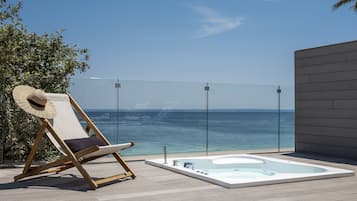 Un fauteuil de jardin en bois, un chapeau de paille, un jacuzzi et une vue dégagée sur l’océan.