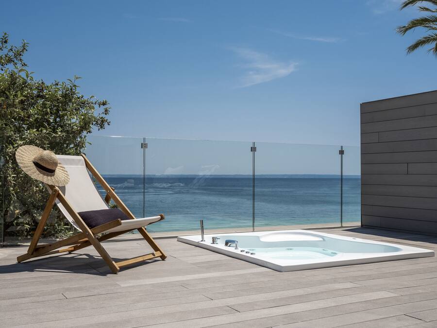 Un fauteuil de jardin en bois, un chapeau de paille, un jacuzzi et une vue dégagée sur l’océan.