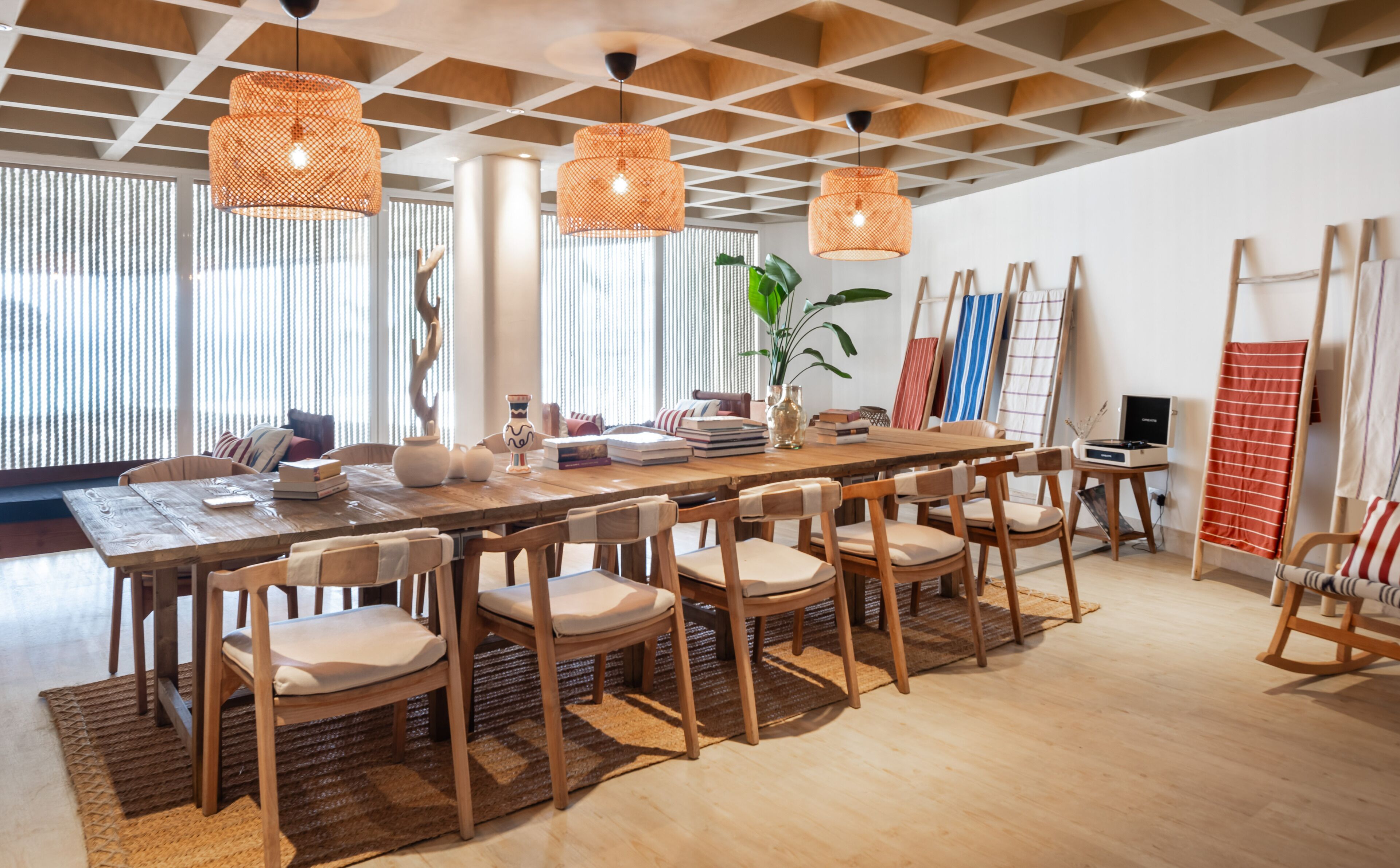A spacious dining area with a long wooden table, multiple chairs, and hanging orange lamps.